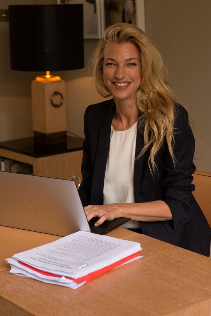 Nicole Junkermann sorride mentre lavora al laptop a una scrivania, con documenti accanto e una lampada